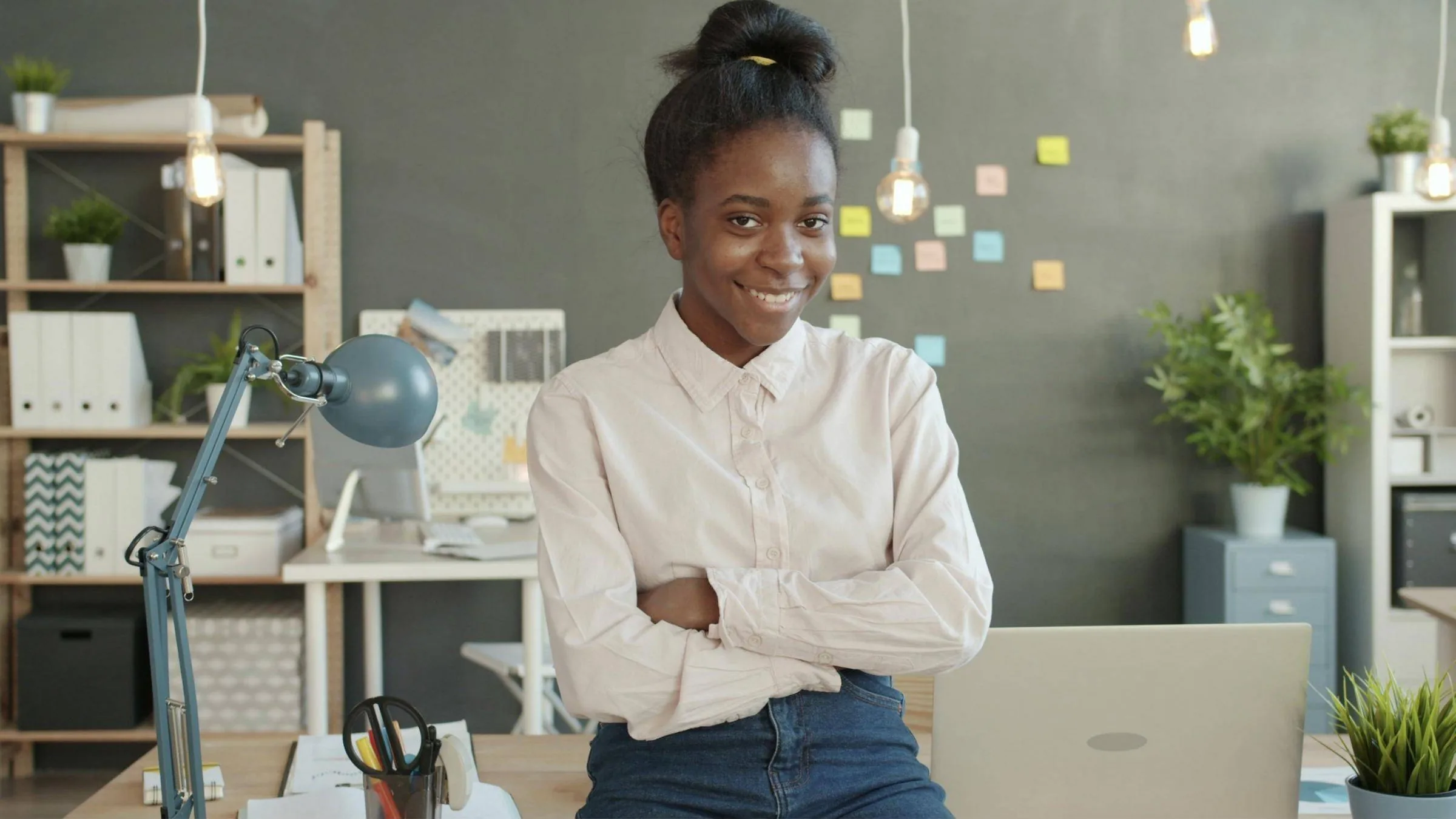 A smiling young professional with arms folded in a bright, modern office