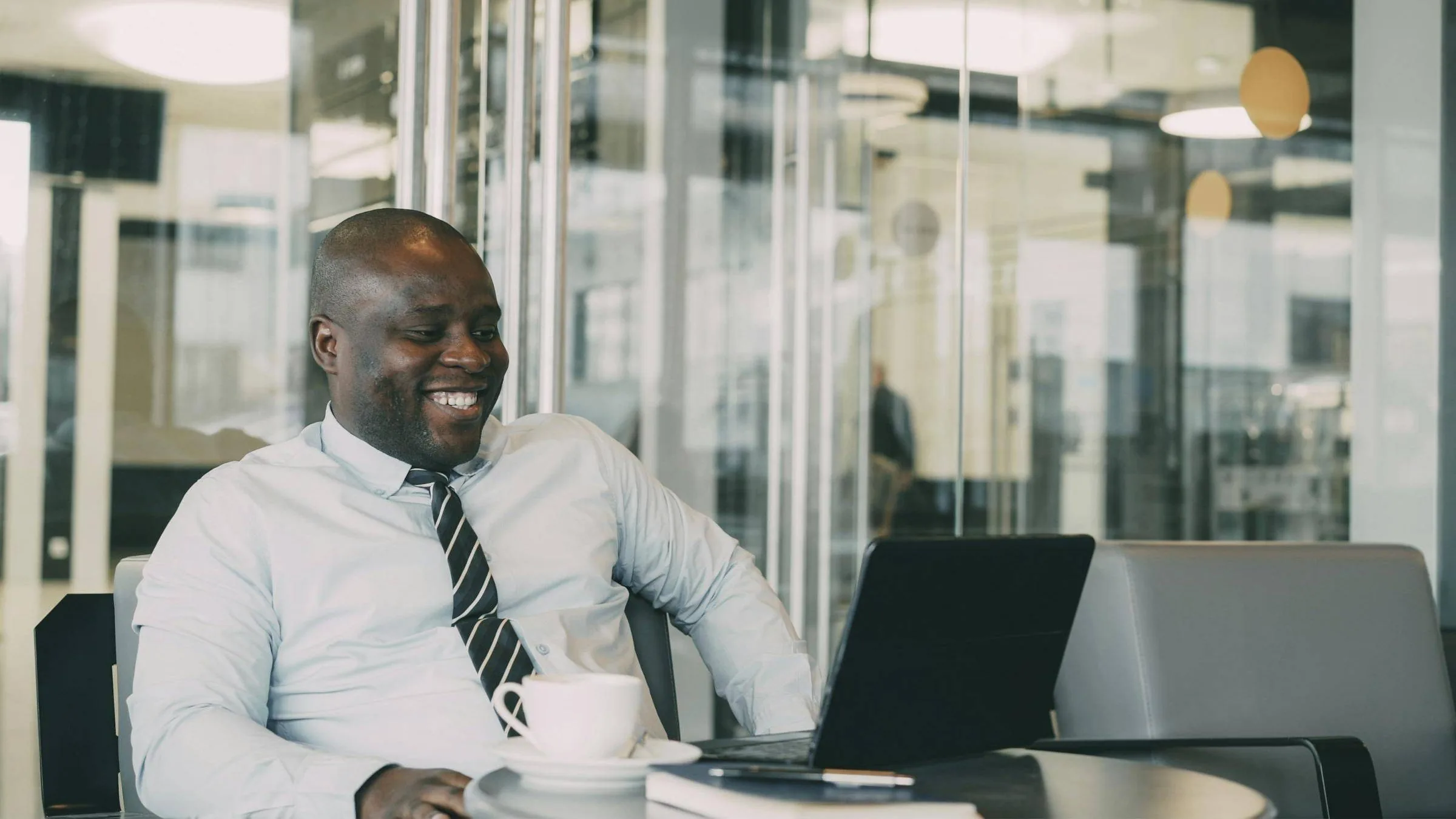 A smiling professional working on a laptop in a bright, glass-walled office