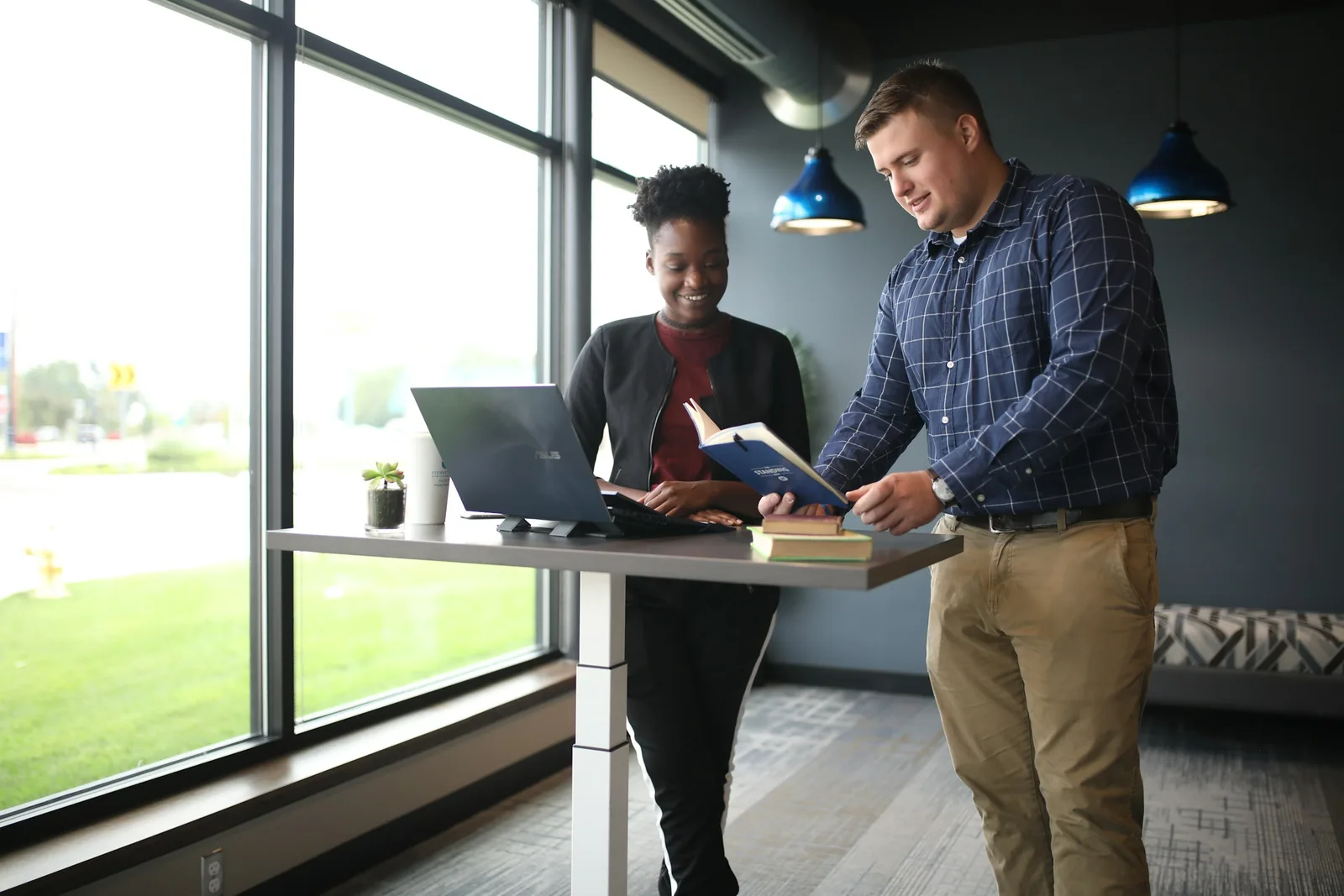 Two colleagues reviewing a document together at a standing desk by a window